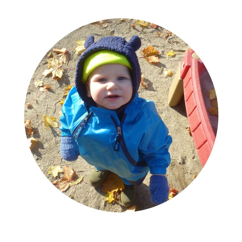 A toddler standing in the sand and looking up at the camera
