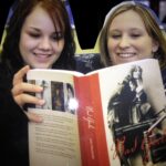 Two young mothers looking at a school textbook and smiling