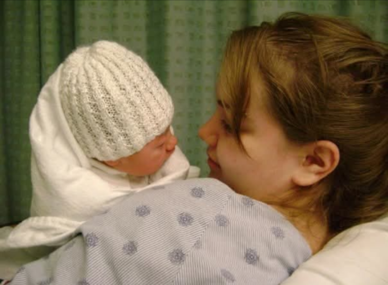 Young mother looking at newborn infant with white knit cap on