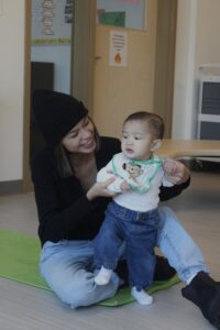Young mother sitting on floor holding up an infant standing in front of her
